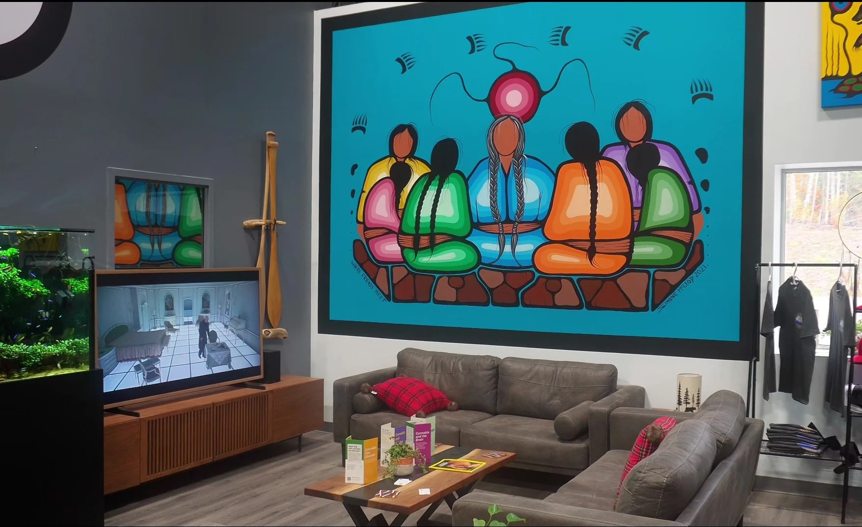 View of entry lounge, there's a large wall mural done in traditional Indigenous art. Part of the aquarium is visible on the left hand side, with a TV and stand beside it. Couches and table are visible.